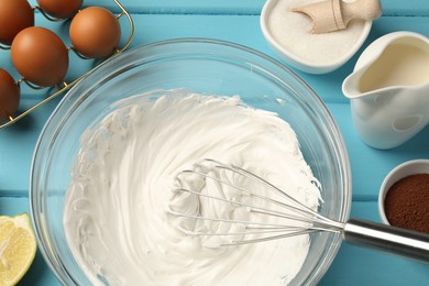 Photo of Whisk with whipped cream, eggs and other products on light blue wooden table, flat lay