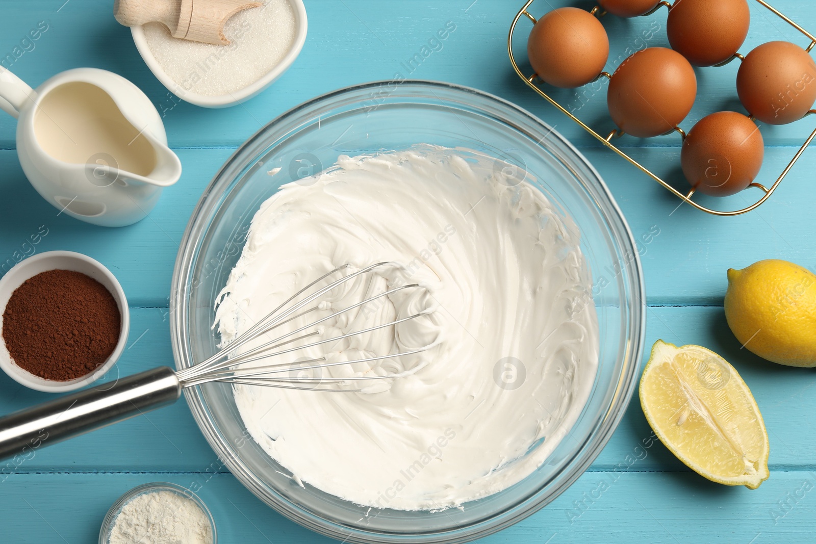 Whisk with whipped cream, eggs and other products on light blue wooden table, flat lay Photo of Whisk with whipped cream, eggs and other products on light blue wooden table, flat lay
