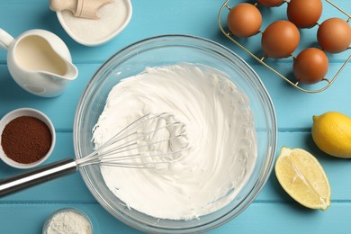 Photo of Whisk with whipped cream, eggs and other products on light blue wooden table, flat lay