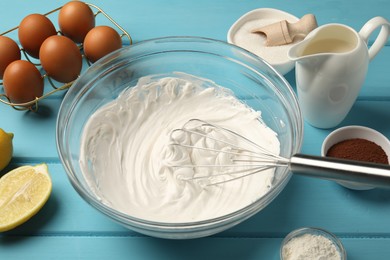 Photo of Whisk with whipped cream, eggs and other products on light blue wooden table, closeup