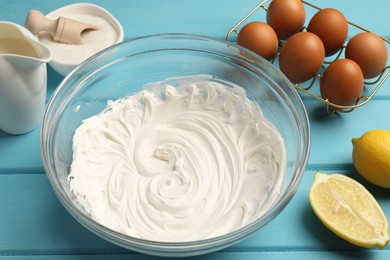 Photo of Whipped cream in bowl, eggs and other products on light blue wooden table, closeup