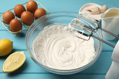 Photo of Hand mixer with whipped cream, eggs and other products on light blue wooden table, closeup