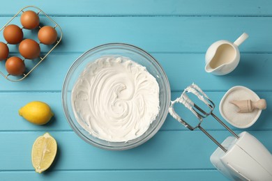Photo of Hand mixer with whipped cream, eggs and other products on light blue wooden table, flat lay