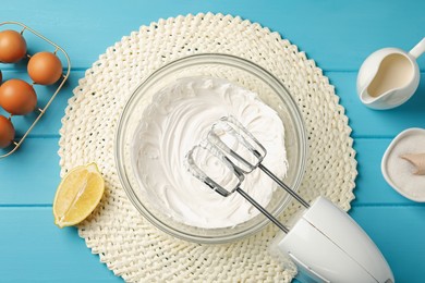 Photo of Hand mixer with whipped cream, eggs and other products on light blue wooden table, flat lay