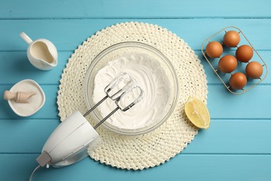Photo of Hand mixer with whipped cream, eggs and other products on light blue wooden table, flat lay