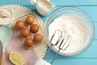 Photo of Hand mixer with whipped cream, eggs and other products on light blue wooden table, flat lay