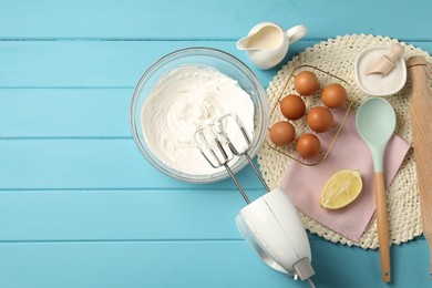 Photo of Hand mixer with whipped cream, eggs and other products on light blue wooden table, flat lay. Space for text
