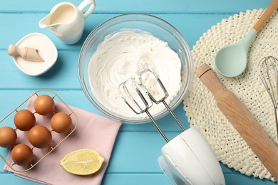 Photo of Hand mixer with whipped cream, eggs and other products on light blue wooden table, flat lay