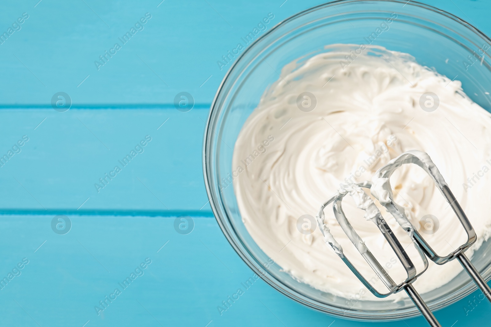 Whisks and whipped cream in bowl on light blue wooden table, top view. Space for text Photo of Whisks and whipped cream in bowl on light blue wooden table, top view. Space for text