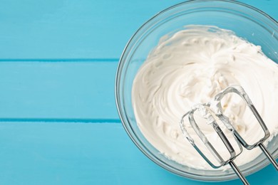 Photo of Whisks and whipped cream in bowl on light blue wooden table, top view. Space for text