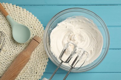 Photo of Whisks, whipped cream in bowl, rolling pin and spoon on light blue wooden table, flat lay