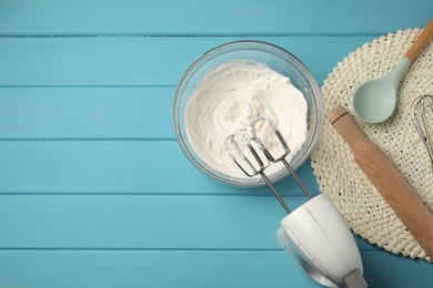 Photo of Hand mixer, whipped cream in bowl, rolling pin and spoon on light blue wooden table, flat lay. Space for text