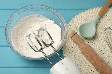 Photo of Hand mixer, whipped cream in bowl, rolling pin and spoon on light blue wooden table, above view