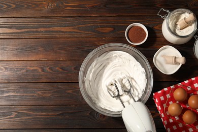 Photo of Hand mixer with whipped cream, eggs and other products on wooden table, flat lay. Space for text