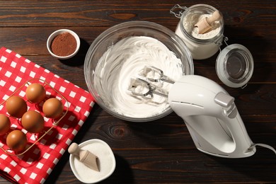 Photo of Hand mixer with whipped cream, eggs and other products on wooden table, flat lay