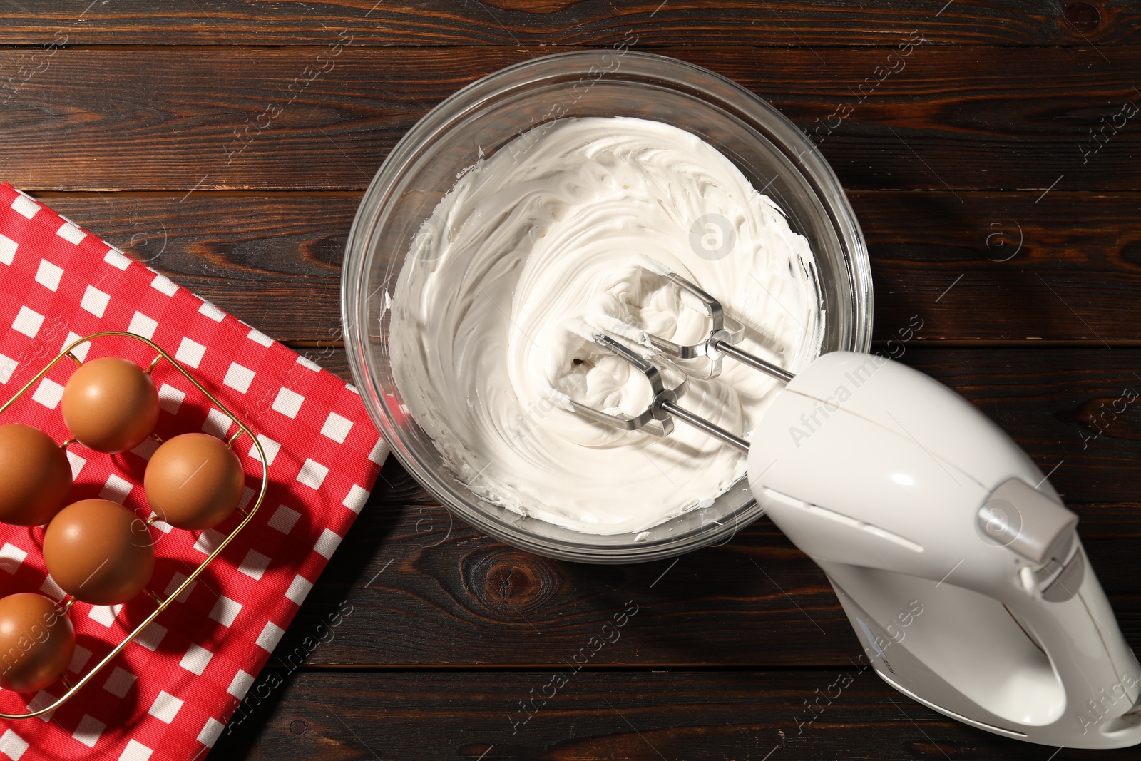 Hand mixer, whipped cream in bowl and eggs on wooden table, flat lay Photo of Hand mixer, whipped cream in bowl and eggs on wooden table, flat lay