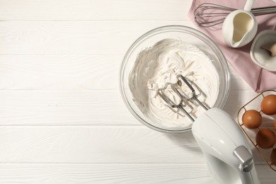 Photo of Hand mixer with whipped cream, eggs and other products on white wooden table, flat lay. Space for text