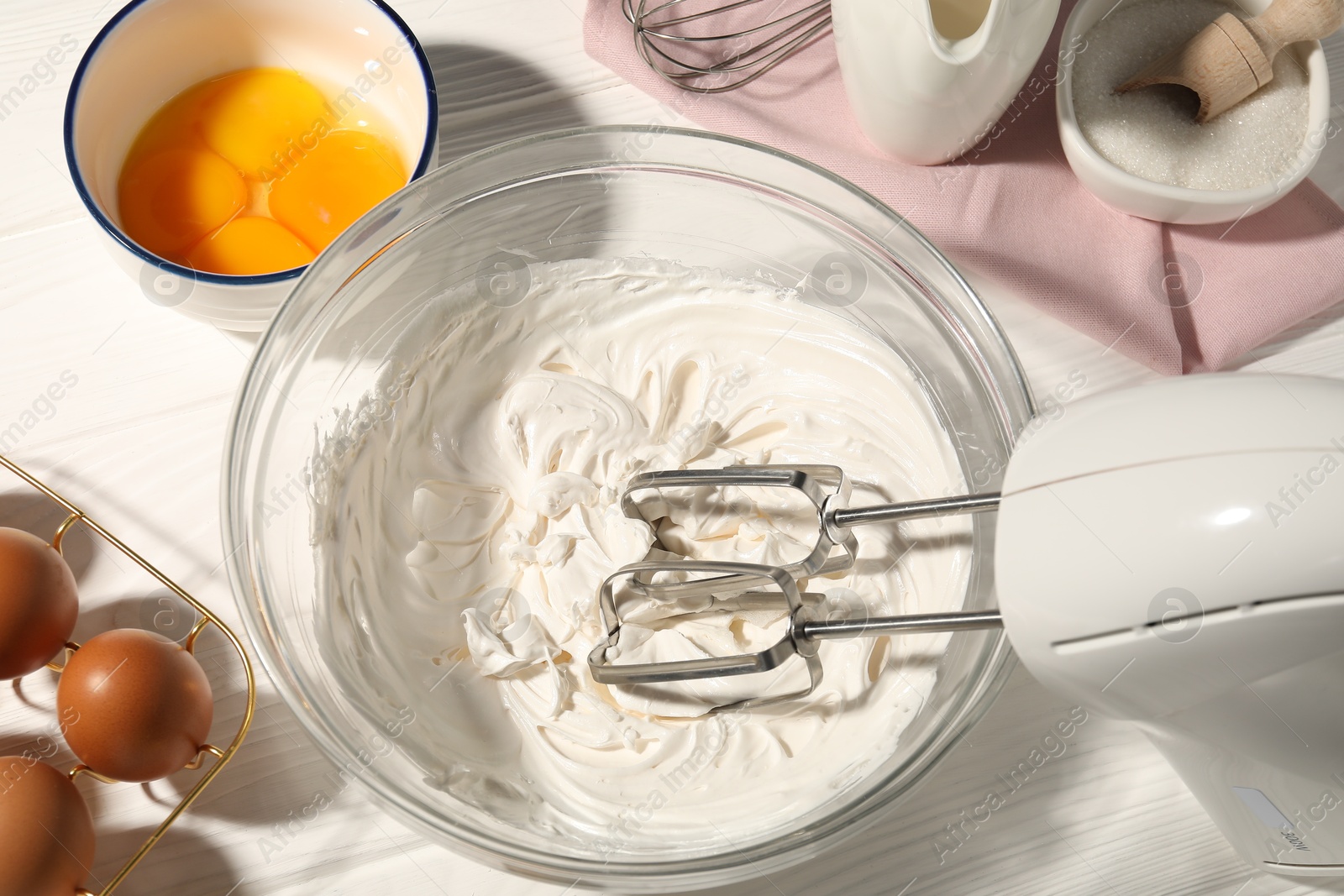 Hand mixer with whipped cream, eggs and other products on white wooden table, flat lay Photo of Hand mixer with whipped cream, eggs and other products on white wooden table, flat lay