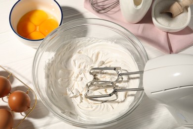 Photo of Hand mixer with whipped cream, eggs and other products on white wooden table, flat lay