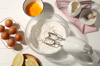 Photo of Hand mixer with whipped cream, eggs and other products on white wooden table, flat lay