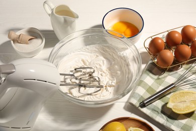 Photo of Hand mixer with whipped cream, eggs and other products on white wooden table