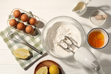 Photo of Hand mixer with whipped cream, eggs and other products on white wooden table, flat lay