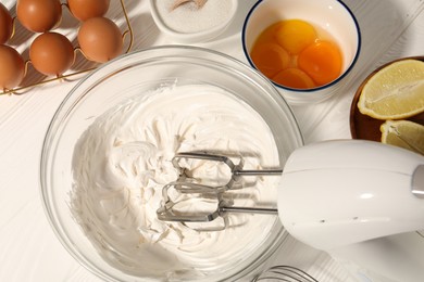 Photo of Hand mixer with whipped cream, eggs and other products on white wooden table, flat lay