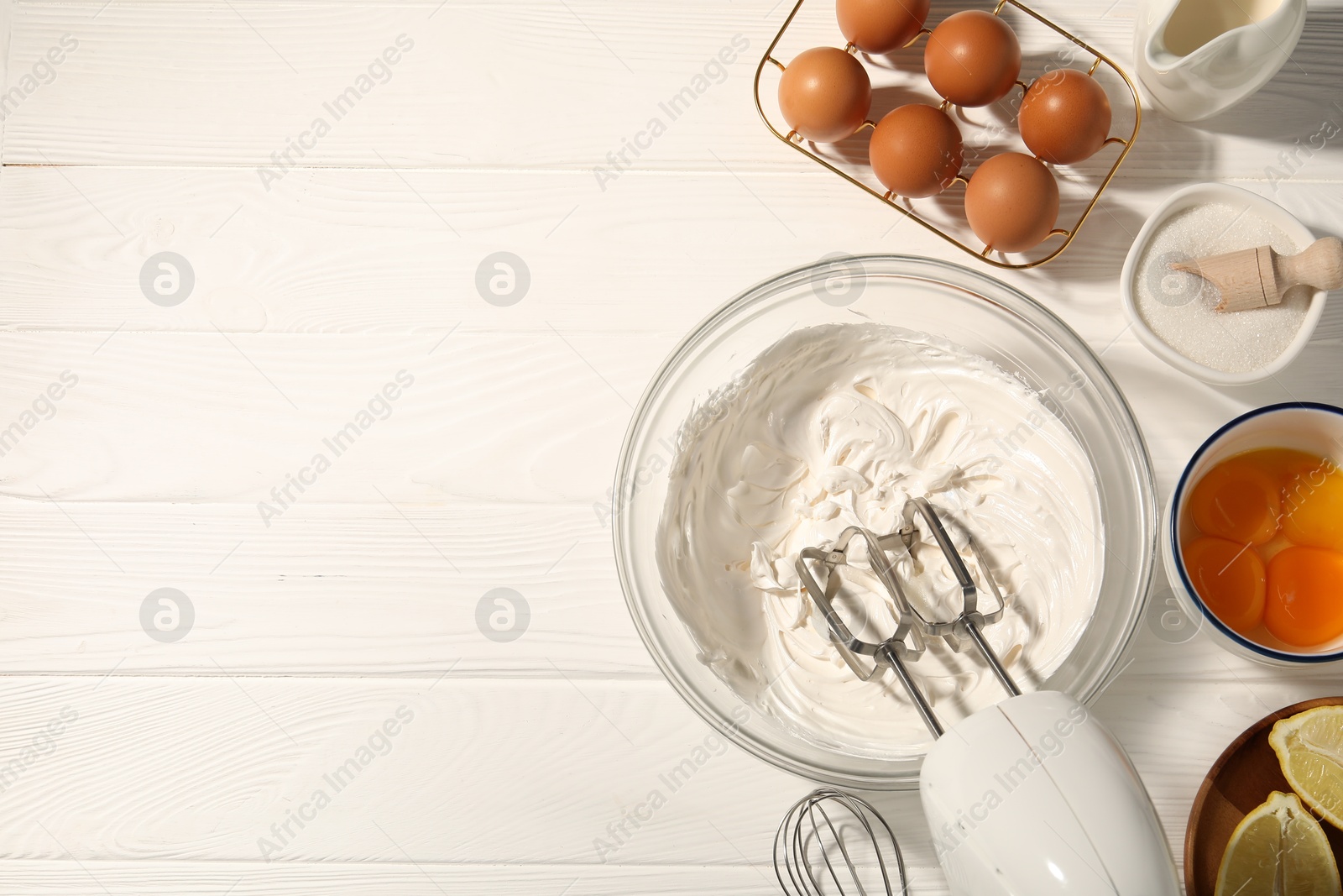 Hand mixer with whipped cream, eggs and other products on white wooden table, flat lay. Space for text Photo of Hand mixer with whipped cream, eggs and other products on white wooden table, flat lay. Space for text