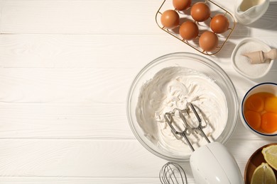Photo of Hand mixer with whipped cream, eggs and other products on white wooden table, flat lay. Space for text