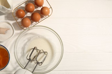 Photo of Hand mixer, egg whites in bowl, eggs and other products on white wooden table, flat lay. Space for text