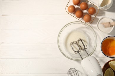 Photo of Hand mixer, egg whites in bowl, eggs and other products on white wooden table, flat lay. Space for text