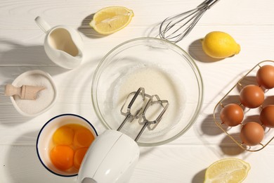 Photo of Hand mixer, egg whites in bowl, eggs and other products on white wooden table, flat lay