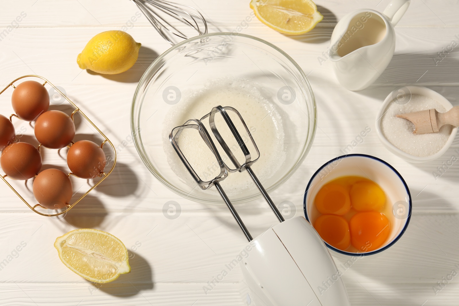 Hand mixer, egg whites in bowl, eggs and other products on white wooden table, flat lay Photo of Hand mixer, egg whites in bowl, eggs and other products on white wooden table, flat lay