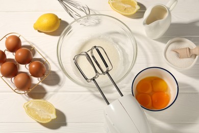 Photo of Hand mixer, egg whites in bowl, eggs and other products on white wooden table, flat lay