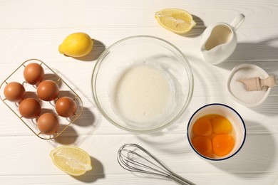 Photo of Whisk, egg whites in bowl, eggs and other products on white wooden table, flat lay