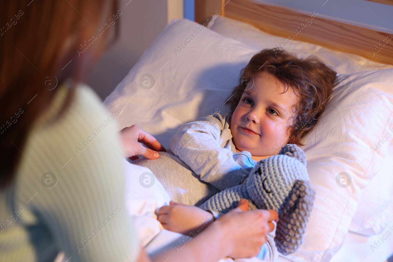Mother putting her little son to sleep at home, selective focus. Bedtime Photo of Mother putting her little son to sleep at home, selective focus. Bedtime