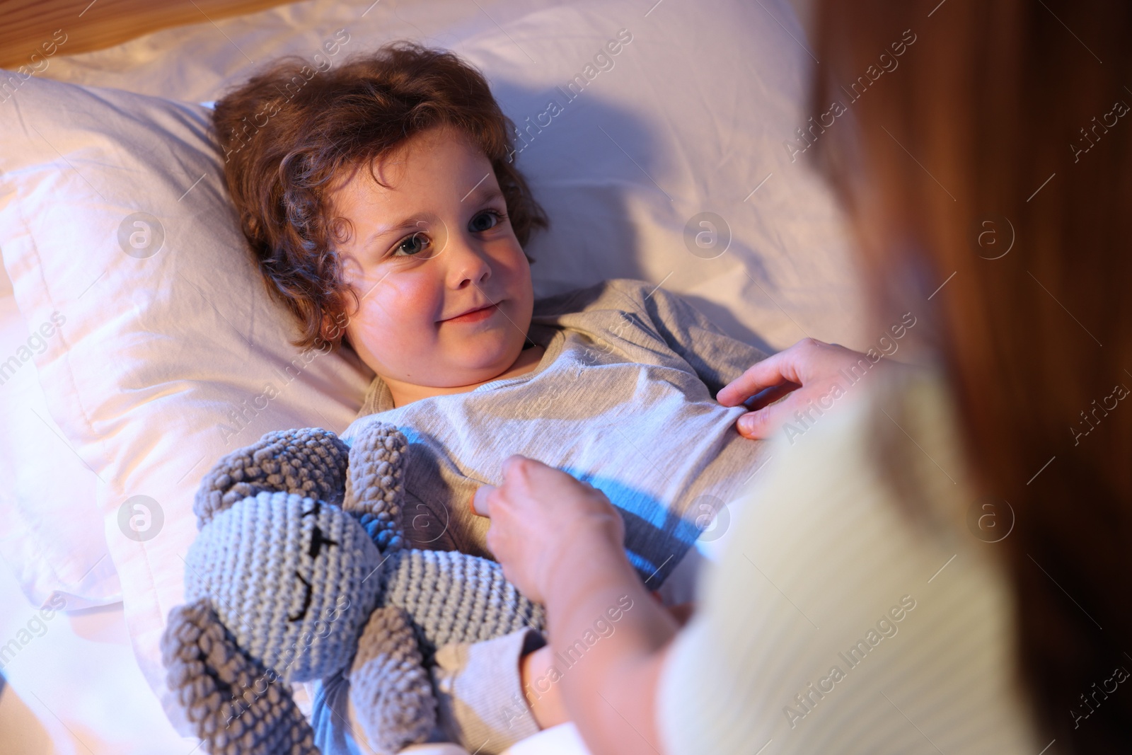 Mother putting her little son to sleep at home, selective focus. Bedtime Photo of Mother putting her little son to sleep at home, selective focus. Bedtime
