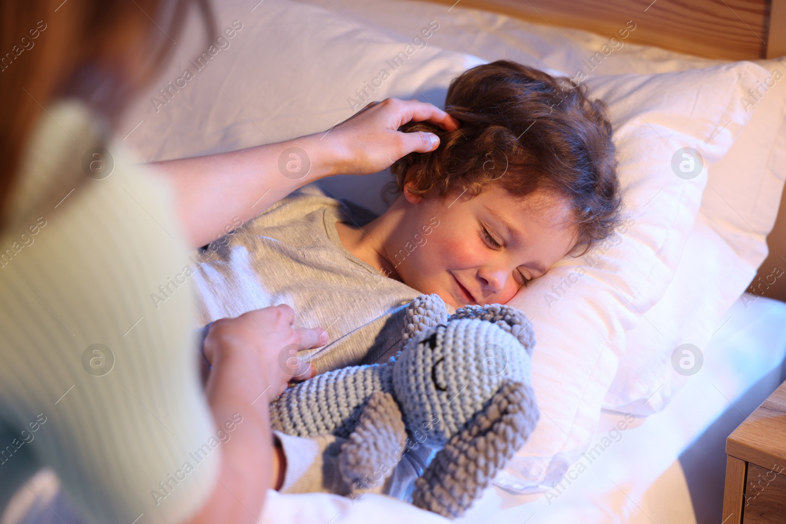Mother putting her little son to sleep at home, selective focus. Bedtime Photo of Mother putting her little son to sleep at home, selective focus. Bedtime
