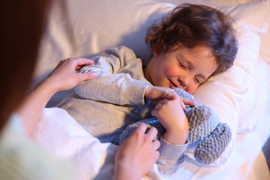 Photo of Mother putting her little son to sleep at home, selective focus. Bedtime