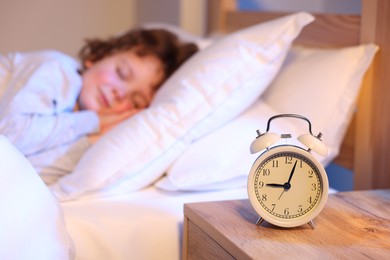Photo of Little boy sleeping in bed at home, focus on alarm clock