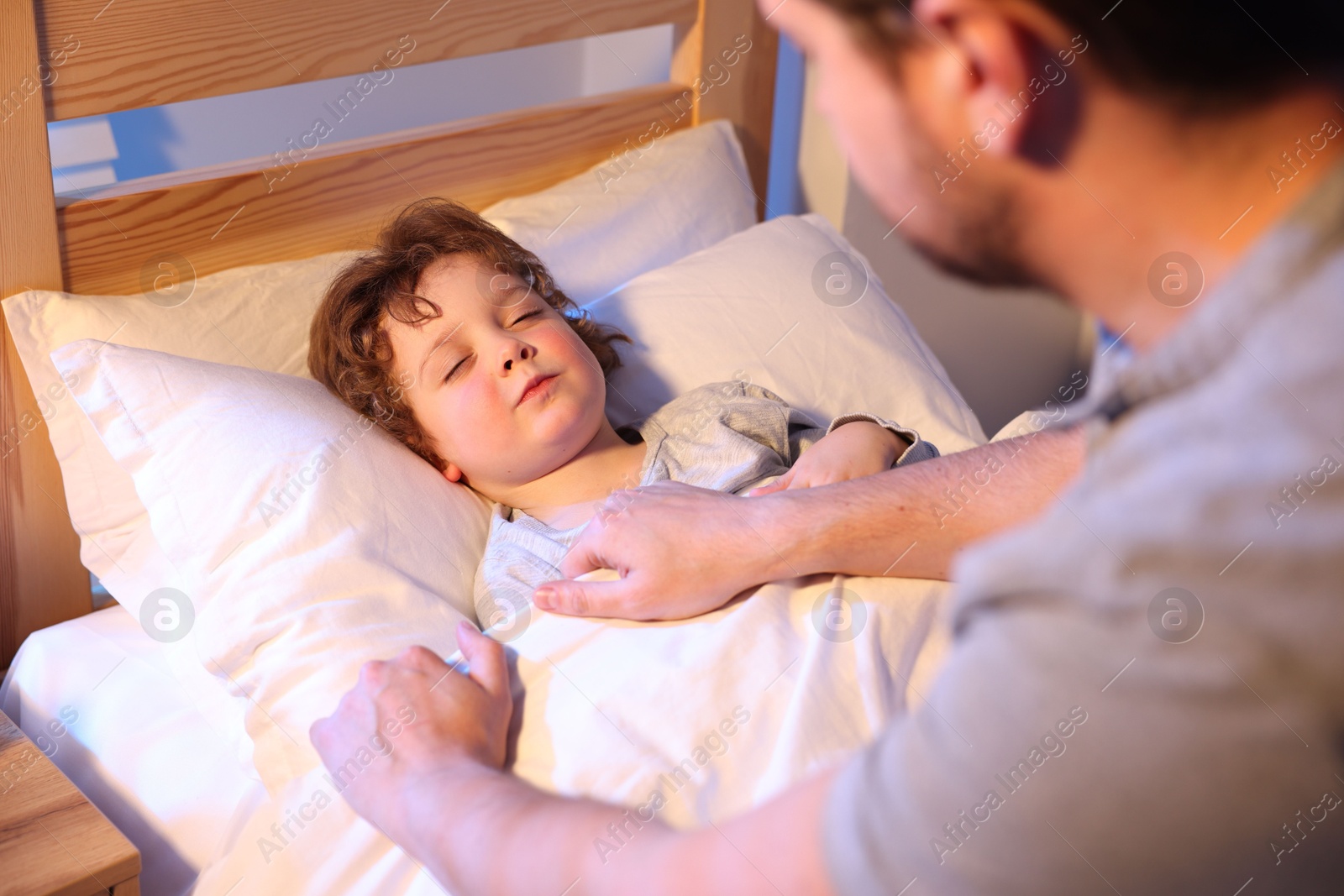 Father putting his little son to sleep at home, selective focus. Bedtime Photo of Father putting his little son to sleep at home, selective focus. Bedtime