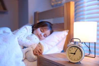 Photo of Little girl sleeping in bed at home, focus on alarm clock