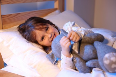 Photo of Smiling little girl with toy in bed at home