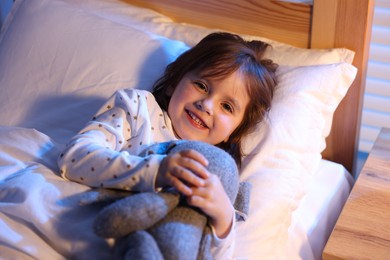 Photo of Smiling little girl with toy in bed at home