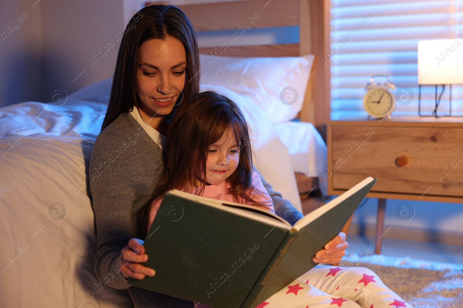 Smiling mother reading bedtime story to her daughter at home Photo of Smiling mother reading bedtime story to her daughter at home