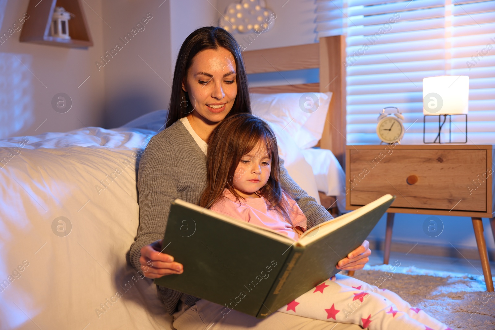 Smiling mother reading bedtime story to her daughter at home Photo of Smiling mother reading bedtime story to her daughter at home