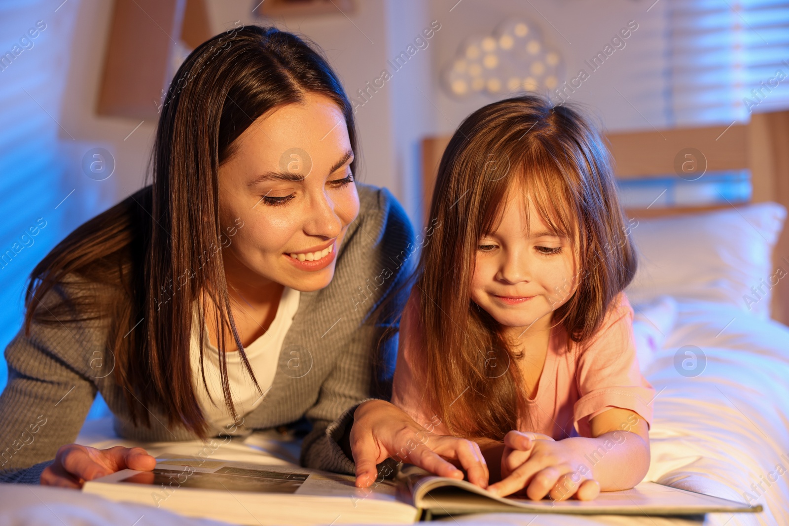 Smiling mother reading bedtime story to her daughter at home Photo of Smiling mother reading bedtime story to her daughter at home