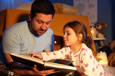 Photo of Father reading bedtime story to his daughter at home