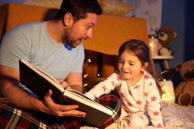 Photo of Emotional father reading bedtime story to his daughter on floor at home