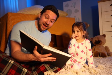 Photo of Emotional father reading bedtime story to his daughter on floor at home